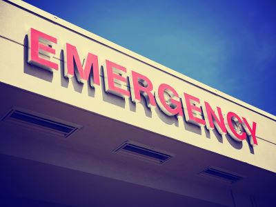 Red sign reading emergency hanging on the face of the hospital building